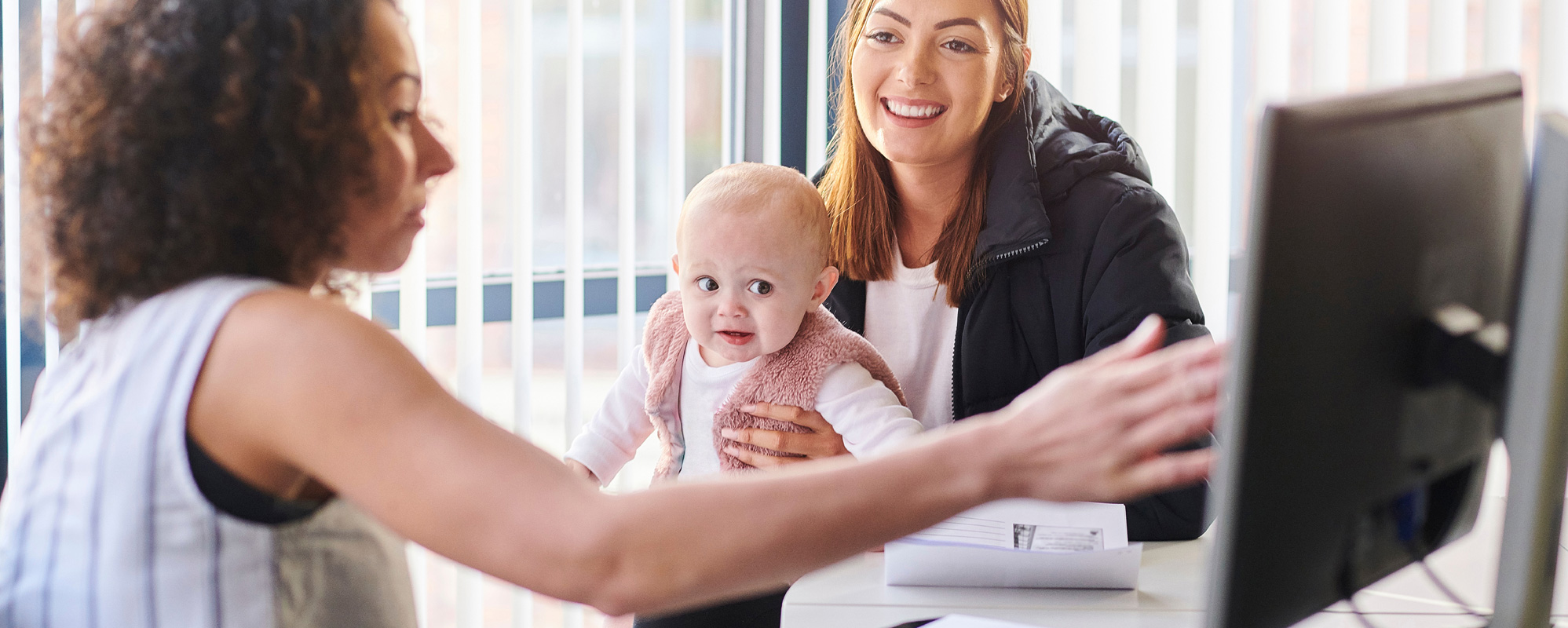 A case manager meeting with a parent and her baby and showing them something on computer.