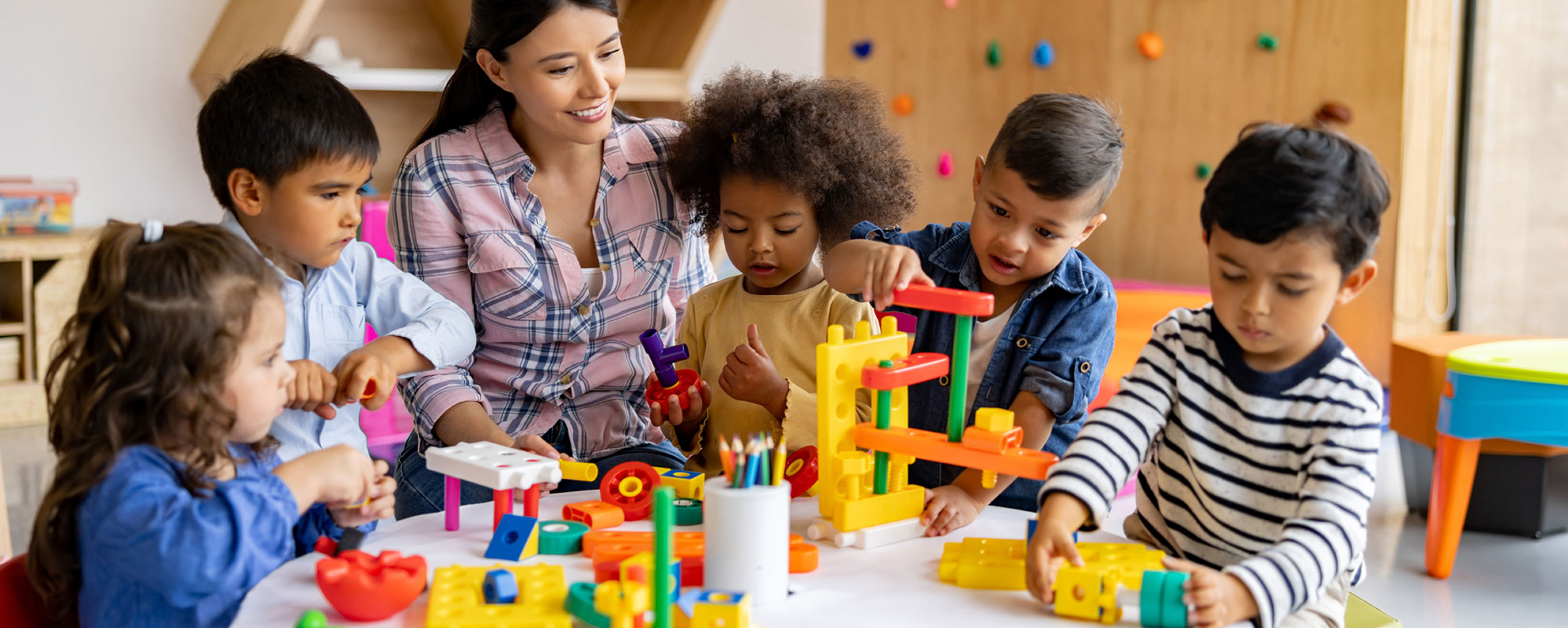 A teacher sitting with children who are playing with toys in class, and smiling at them.