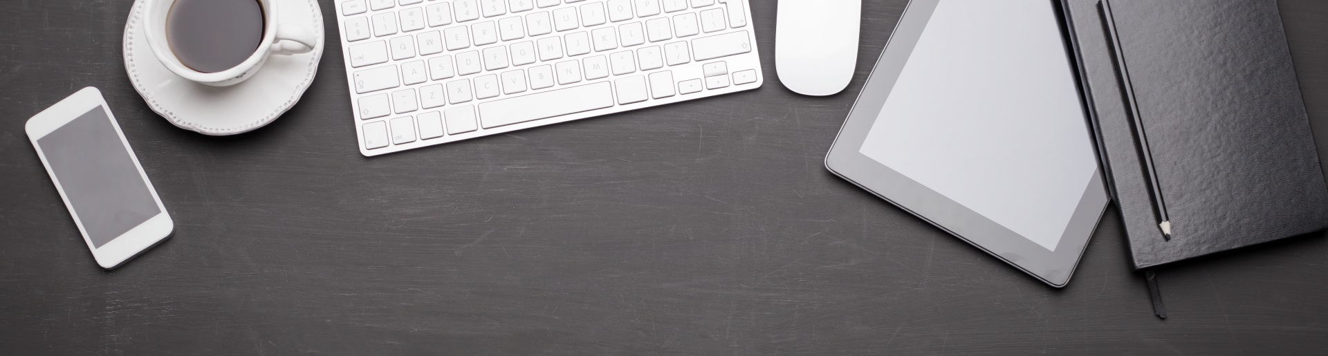 Cup of coffee, iPhone and iPad, as well as other office materials on a black desk.