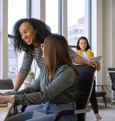 African-American women supervising co-worker at co-worker's computer.